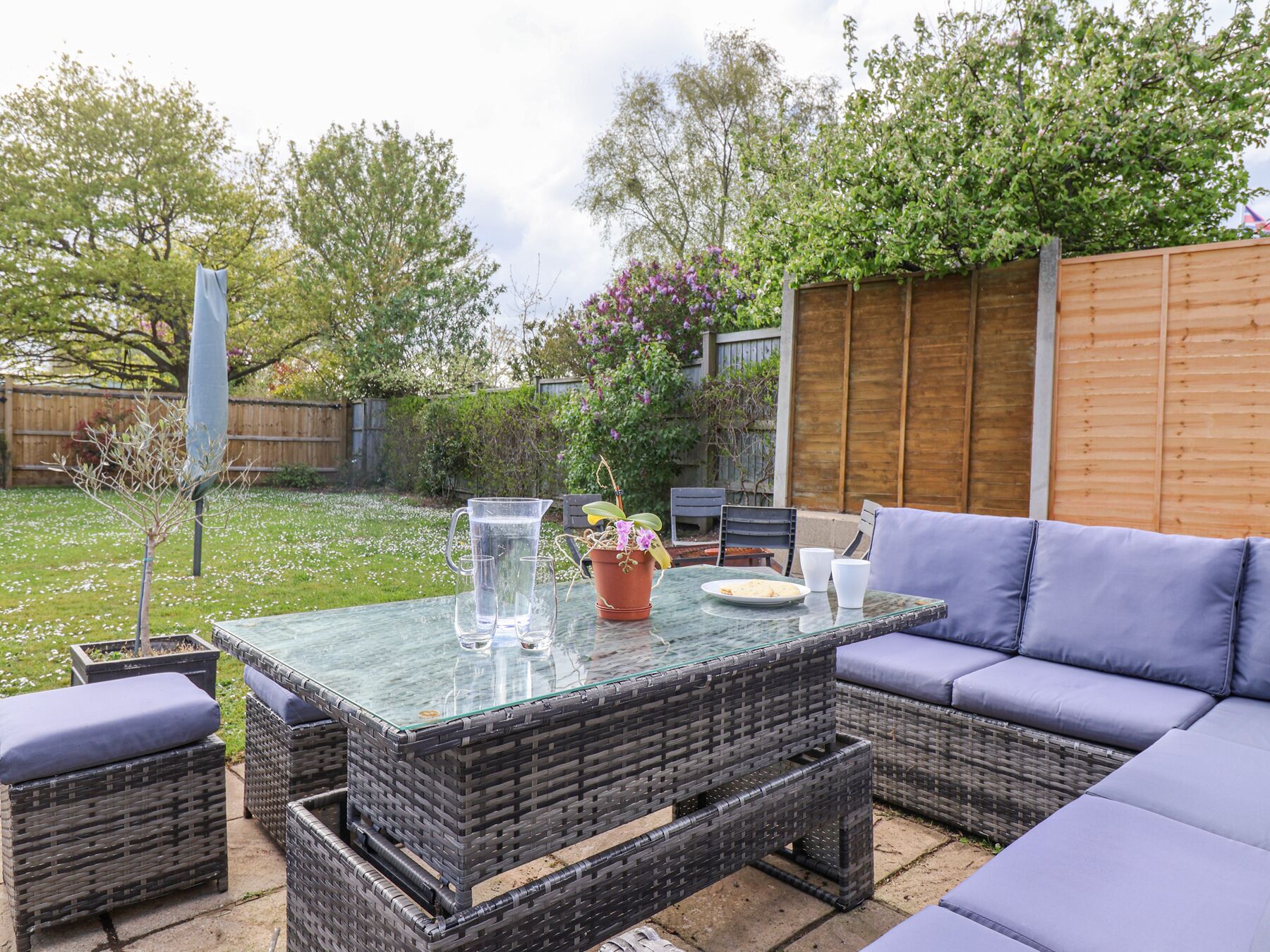 A patio area with wicker furniture, a glass-top table, and a wooden fence in the background.