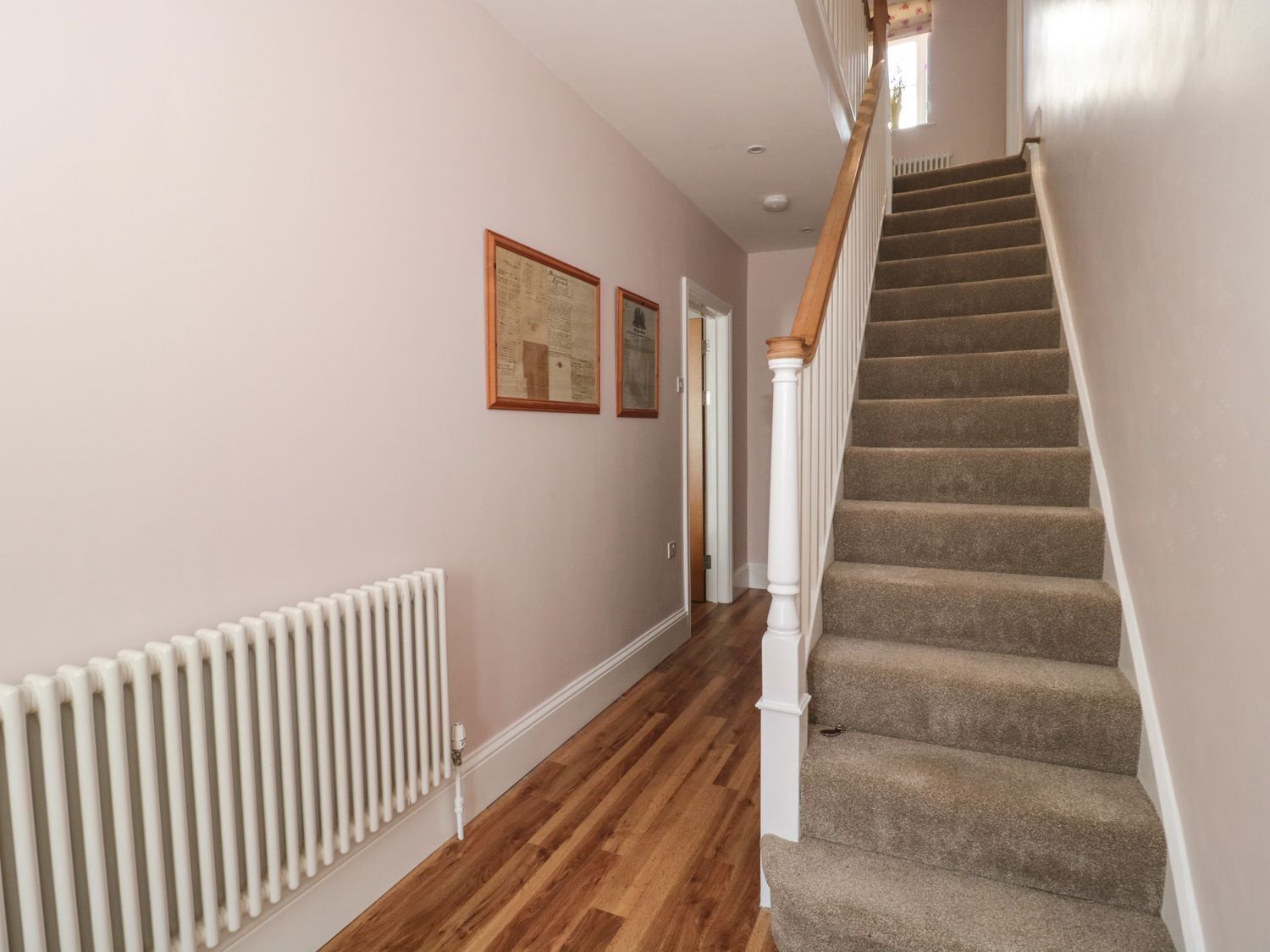 A hallway with a carpeted staircase, wooden handrail, and a white radiator.