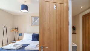 A hotel room with a bed, a wooden door, a hanging light fixture, a towel rack, and a framed picture on the wall.