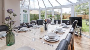 A conservatory dining area with a table set for four, surrounded by chairs, and a vase of flowers on the table.