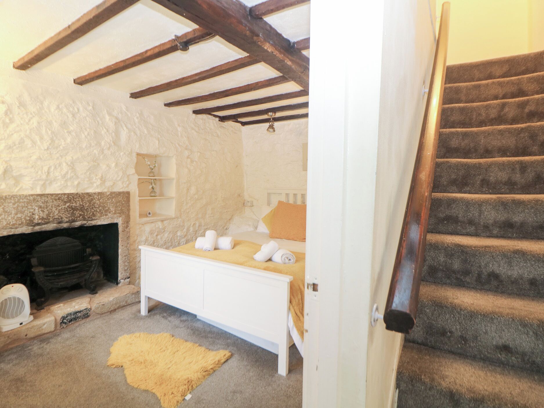 Un dormitorio con pared de piedra, chimenea, cama con manta amarilla y escalera.