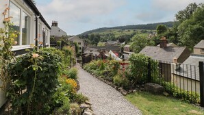 A narrow gravel path leading through a residential area with houses on both sides, surrounded by greenery and a hilly landscape in the background. - Roseville (Matlock)