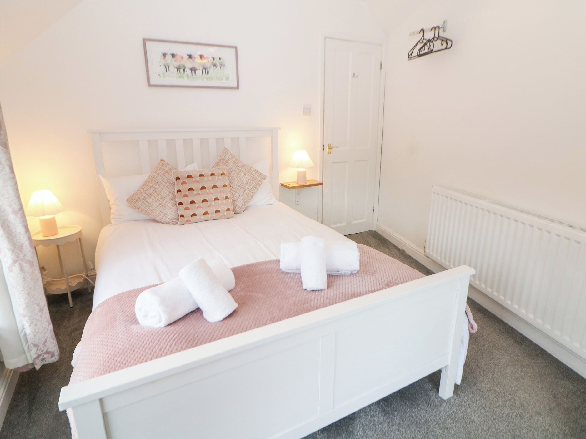 A neatly arranged bedroom with a bed, bedside lamps, a framed picture on the wall, and a door.