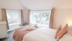 A bedroom with a large bed, two windows, a bedside table, and a view of the outside. - Roseville (Matlock)