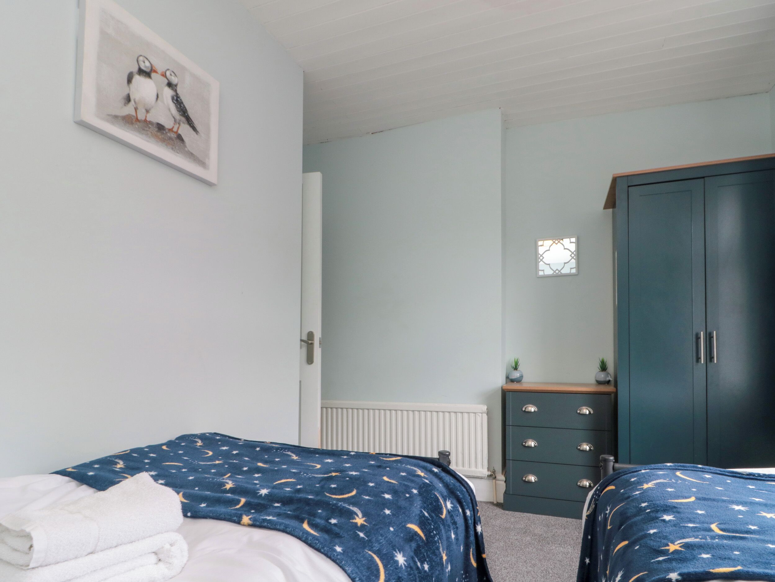 A bedroom with two beds, a dresser, a radiator, and a framed picture on the wall.