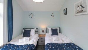 A bedroom with two beds, a nightstand, a lamp, a clock, and a framed picture on the wall.