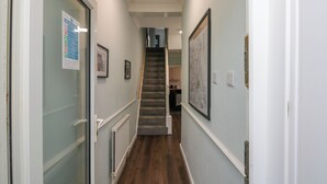 A hallway with a staircase leading to an upper floor, framed pictures on the walls, and a door with a glass panel on the left.