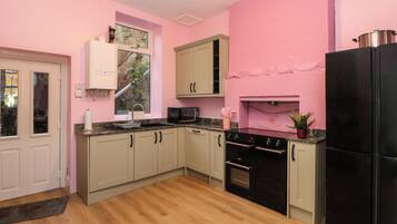 A kitchen with light wood flooring, a black refrigerator, a stove, and a microwave.