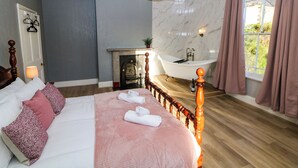 Une chambre à coucher avec un grand lit, une tête de lit en bois, un mur en marbre, une baignoire et une fenêtre avec des rideaux.