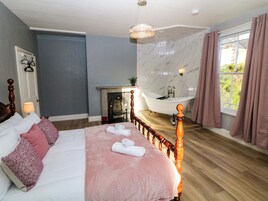 Quarto com cama grande, cabeceira de madeira, parede de mármore, banheira e janela com cortinas.