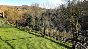 Une pelouse bien entretenue, agrémentée d’une clôture en métal noir, d’arbres et offrant une vue lointaine sur des collines.