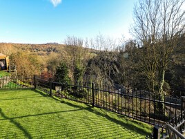 Um gramado bem cuidado, cercado por uma grade de metal preto, com árvores e uma vista distante de colinas.