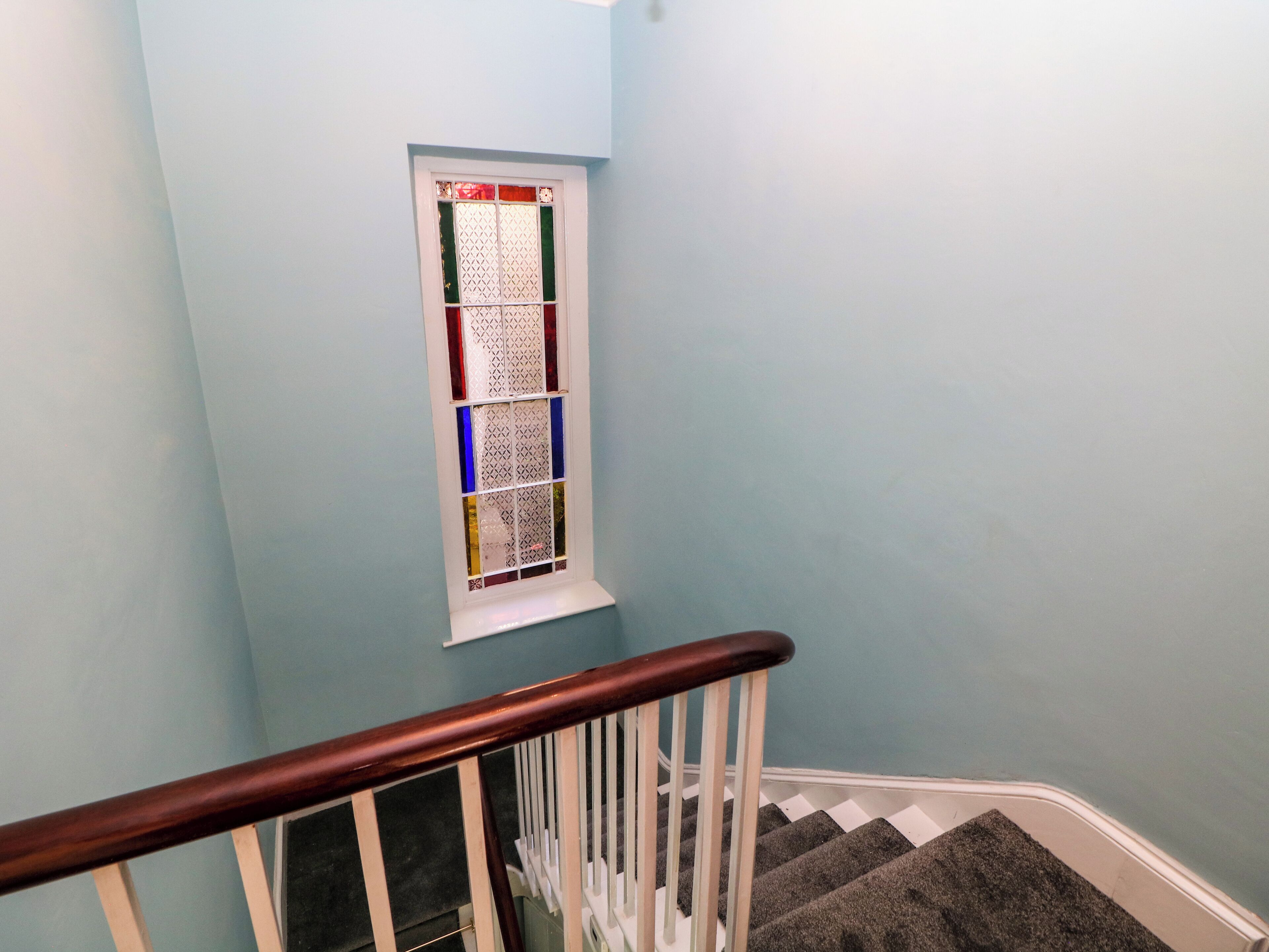 Una escalera con barandilla de madera y una ventana con vidrieras de colores.