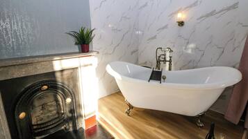 A bathroom with a freestanding bathtub, a marble wall, a small potted plant, and a bottle of champagne on the floor.