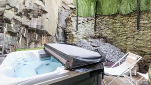 A hot tub in an outdoor setting with a stone wall and greenery. - Gwynfa (Barmouth)