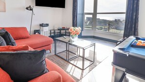 A modern living room with a red sofa, a coffee table, and a large window offering a view of the outdoors. - Gwynfa (Barmouth)