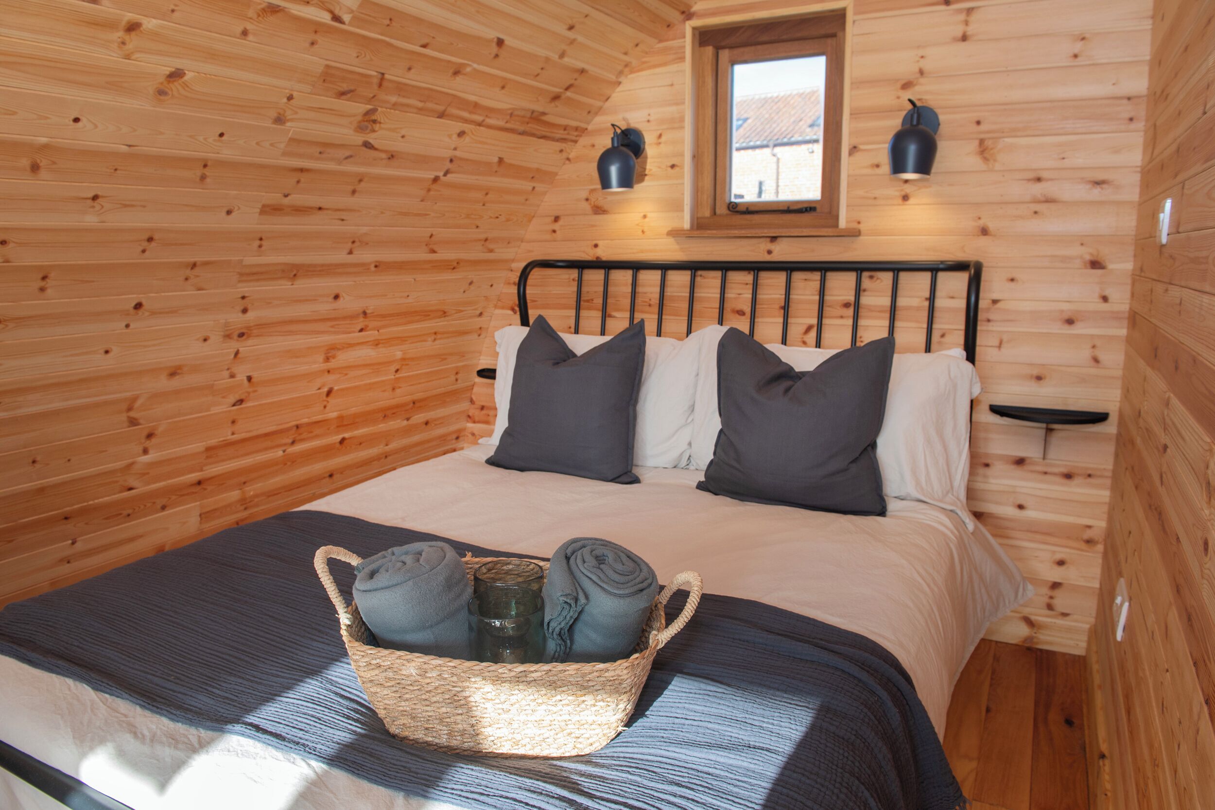 Une chambre confortable, aménagée dans un chalet en bois, avec un lit, des oreillers, une table de chevet et une fenêtre.