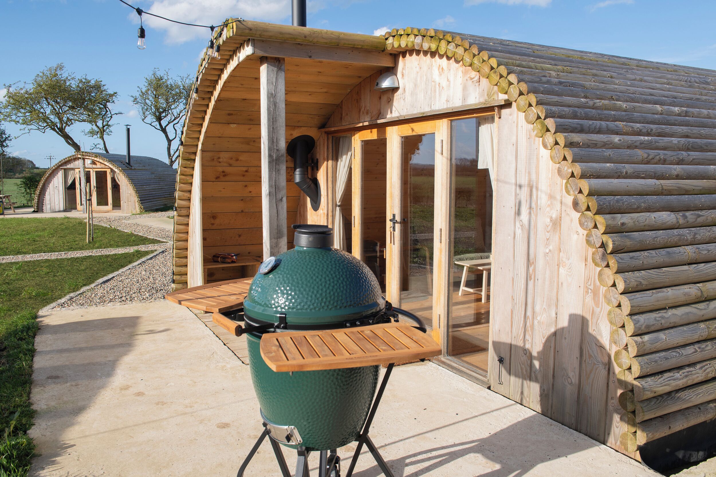 Eine Holzhütte mit einer überdachten Terrasse, einem Grill und einer Glasdoor, die zu einem Außenbereich führt.