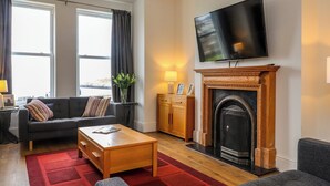 A living room with a fireplace, a sofa, a coffee table, and a television mounted on the wall. - Dolfor (Cemaes Bay)