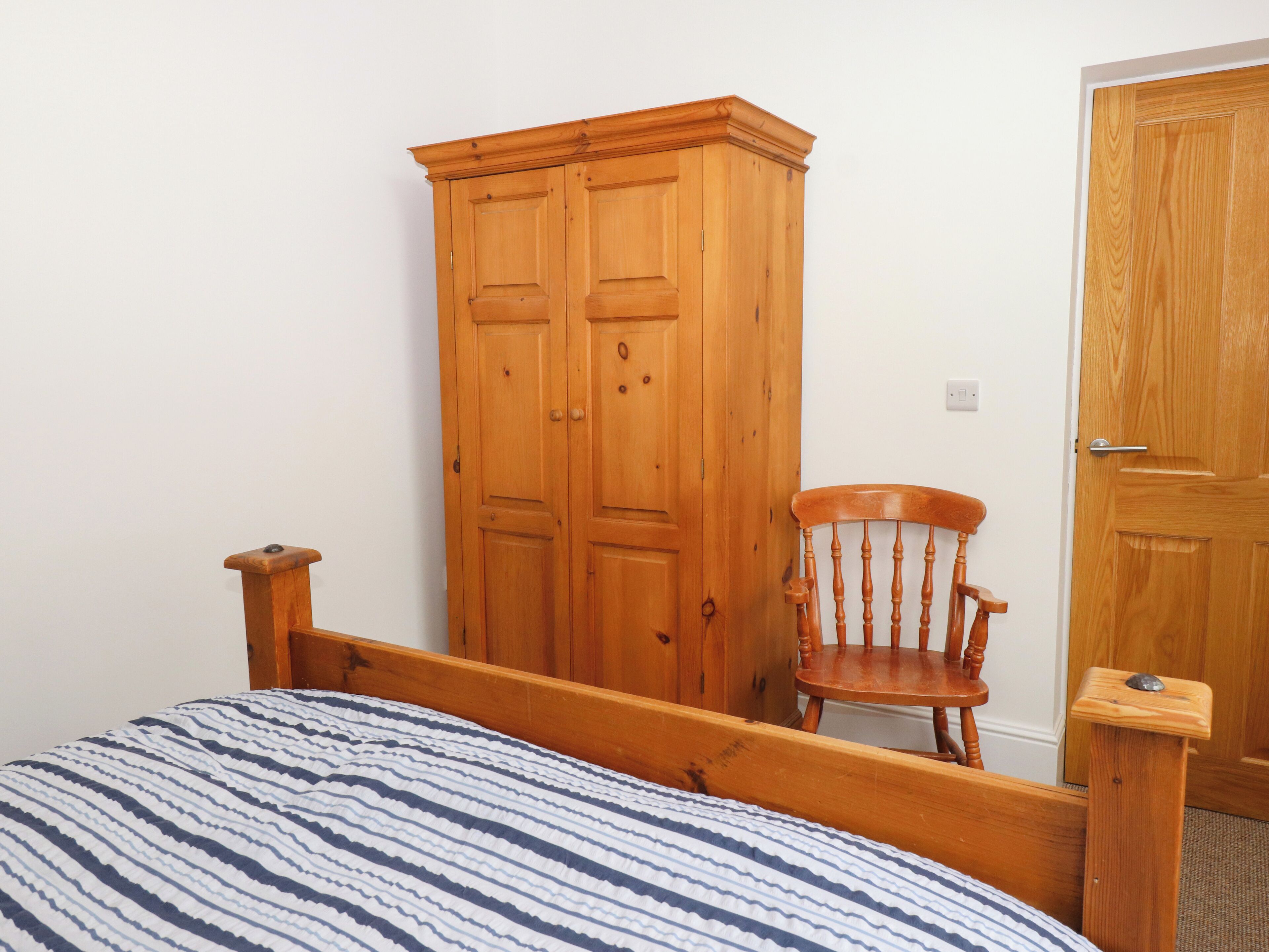 Ein Schlafzimmer mit einem hölzernen Bettgestell, einer gestreiften Bettdecke, einem Holzschrank und einem Holzstuhl.