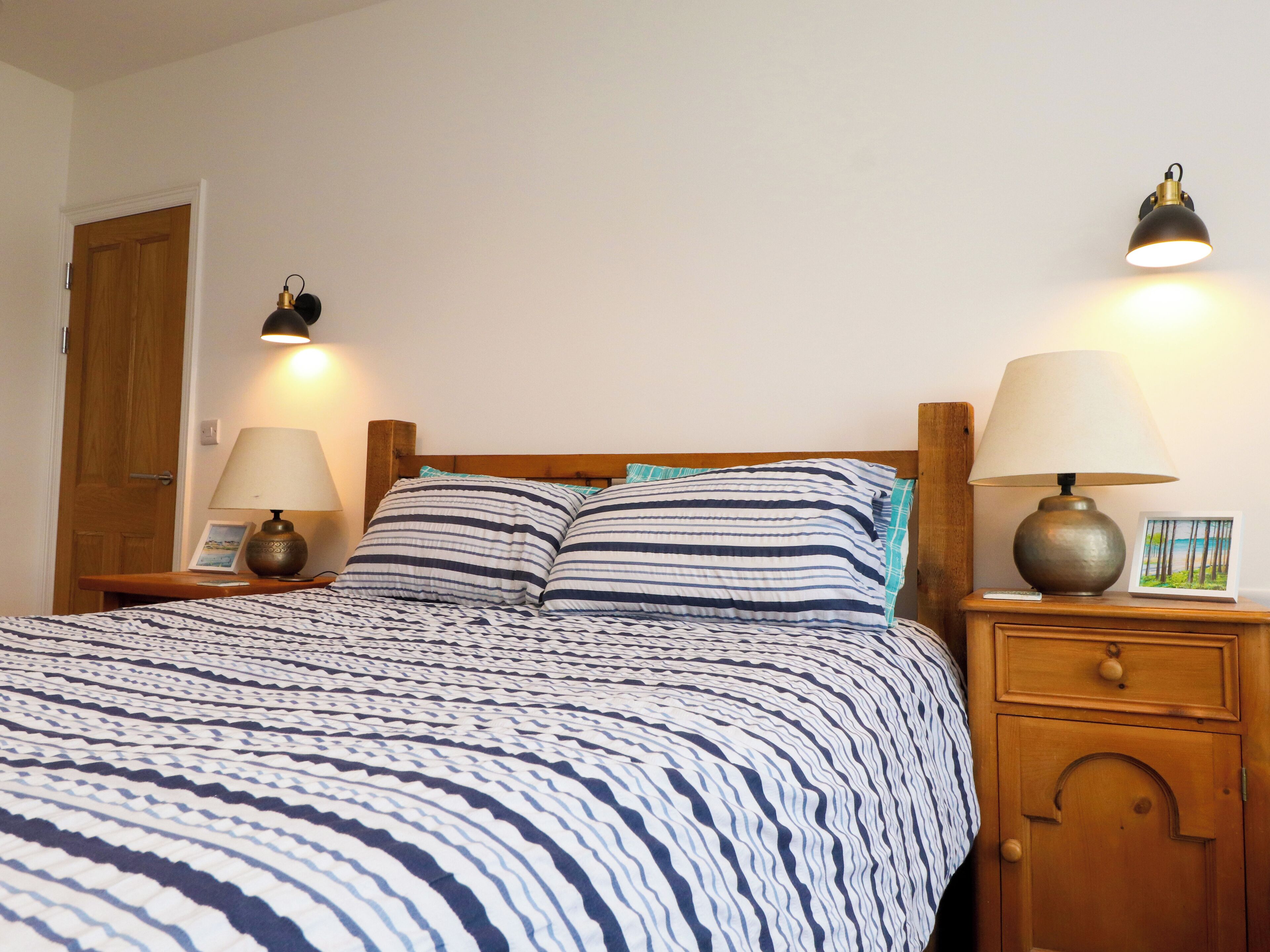 A neatly made bed with striped bedding, two bedside lamps, and a small bedside table with a picture frame.