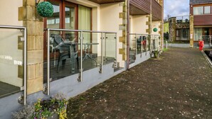 Ein modernes Gebäude mit einem Glasbalkon, Steinsäulen und einem gepflasterten Weg.