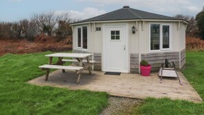 A small, single-story cottage with a white door, a window, and a picnic table. - Berry Bay (Bideford)