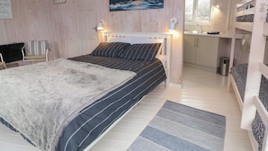 A cozy cabin interior with a bed, a chair, a painting of a sunset, and a small kitchen area. - Berry Bay (Bideford)