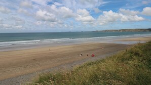 Ein Strand mit blauem Himmel, ruhigem Meer und sanften Hügeln im Hintergrund.