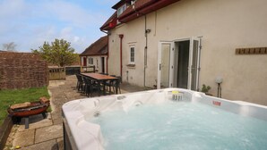 Ett bubbelbad i en trädgård, med ett bord och några stolar, ett trästaket och ett hus med ett rött tak.