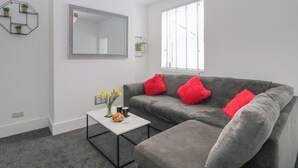Una sala de estar moderna con un sofá gris, cojines rojos, una mesa de centro blanca y un espejo grande en la pared.