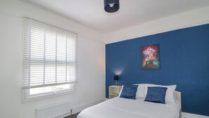 Un dormitorio con una cama, un radiador, una ventana con persianas, una lámpara de pared y un cartel.