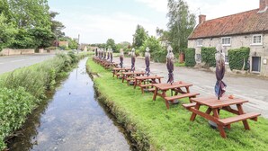 Une rangée de tables de pique-nique le long d’un étroit canal, dans un cadre rural.