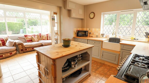 Une cuisine avec un îlot central en bois, un four à micro-ondes, un évier et une cuisinière. Une fenêtre offre une vue sur la verdure à l’extérieur.