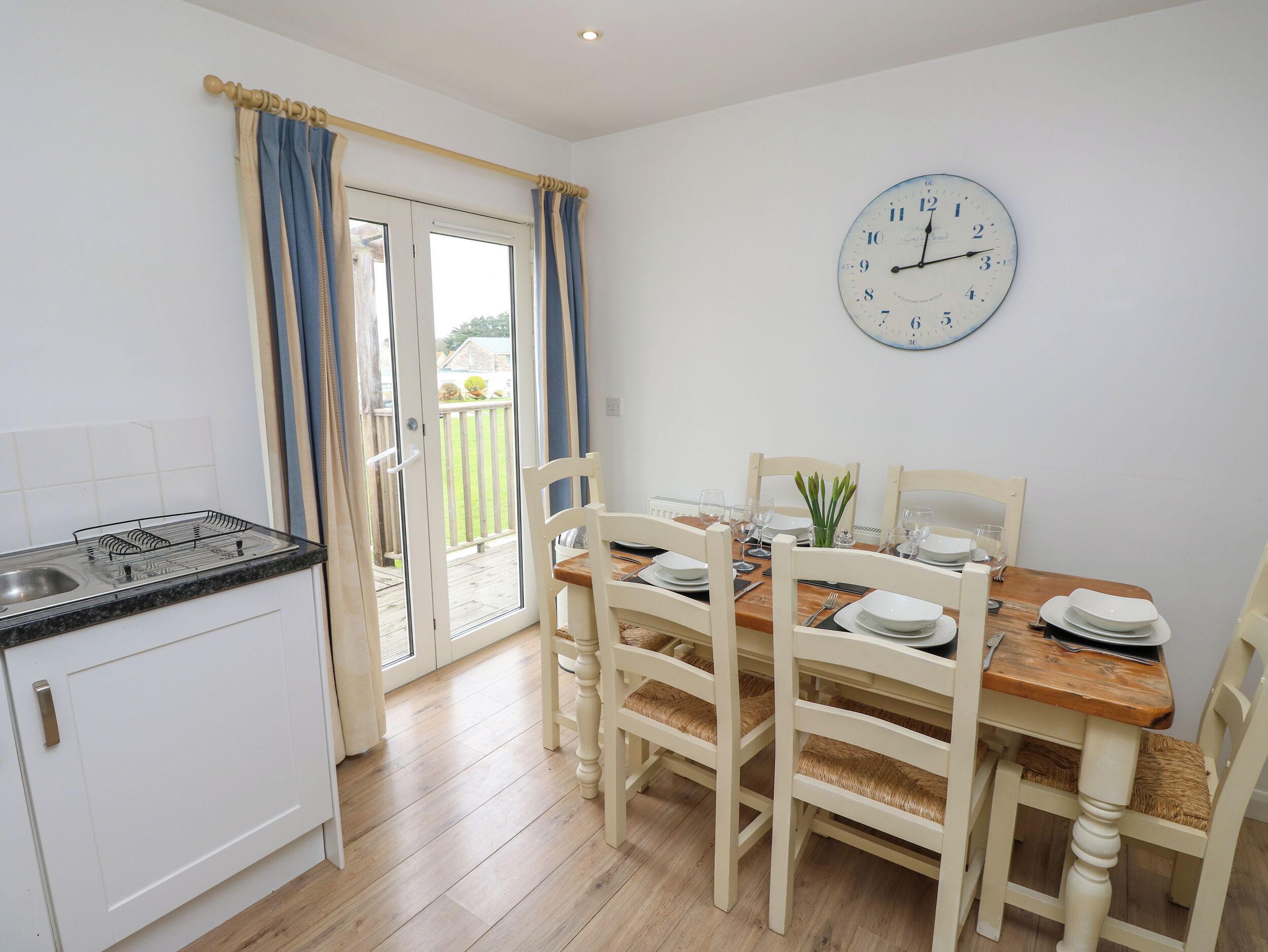 A kitchen with a dining area, a clock on the wall, and a view through the glass door.