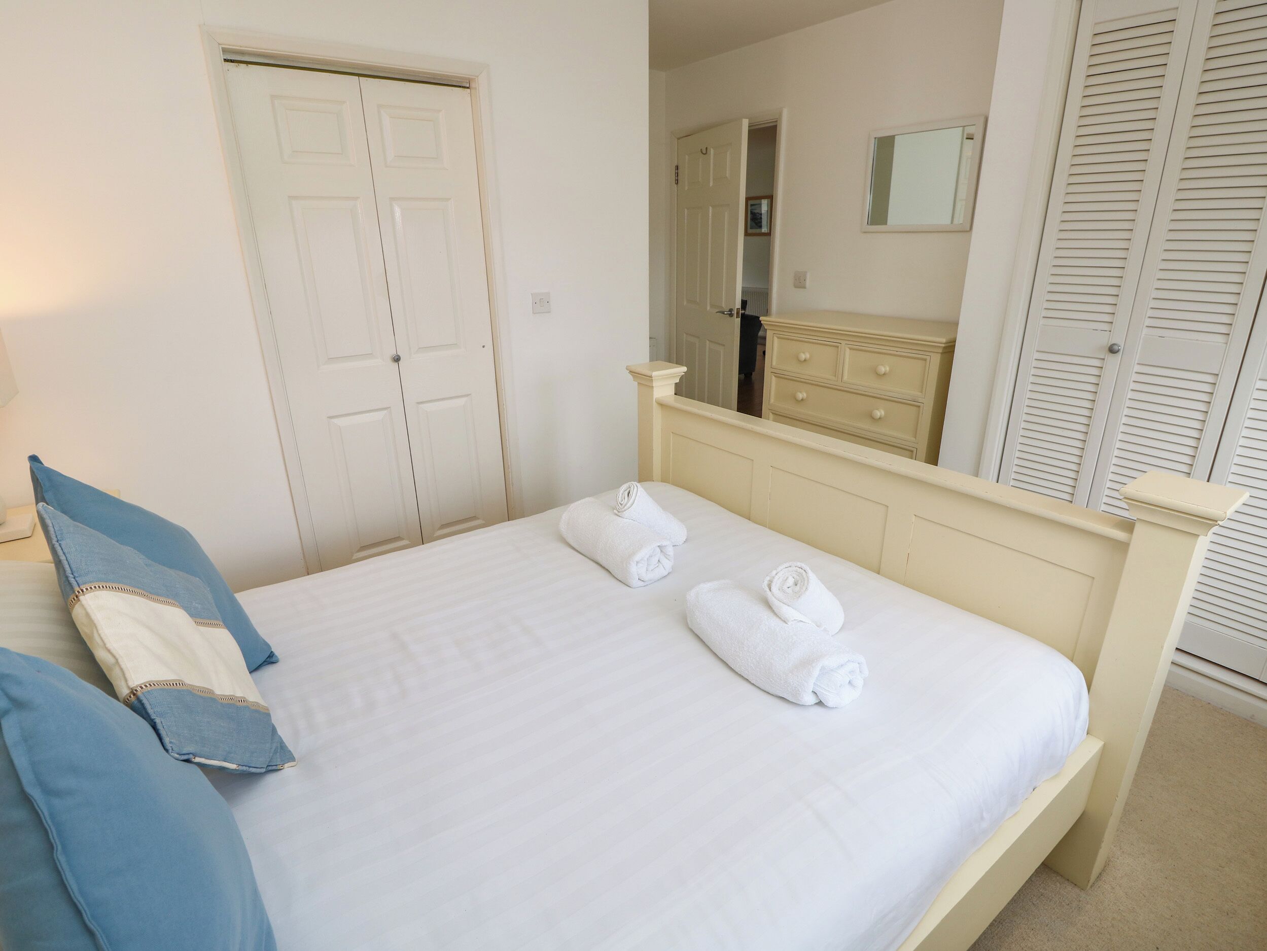 A neatly made bed with white linens and two rolled towels, a blue pillow, and a matching blue pillowcase.