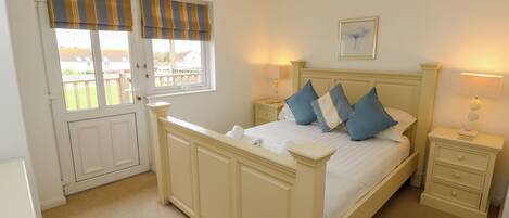 A bedroom with a bed, two bedside tables, a window with curtains, a picture on the wall, and a door leading to a balcony.