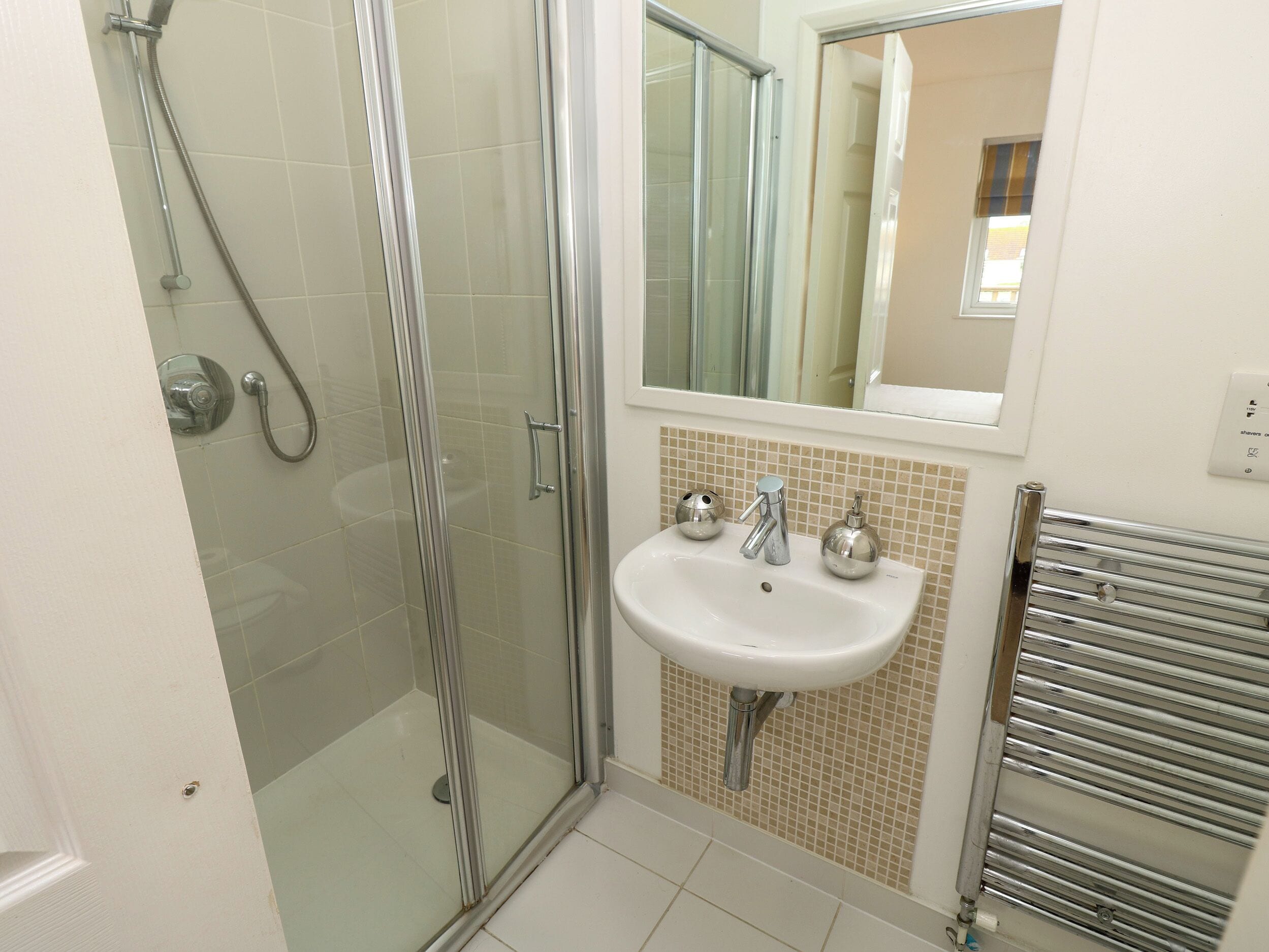 Une salle de bain avec une douche à parois de verre, un lavabo doté de deux distributeurs de savon et un miroir au-dessus du lavabo.