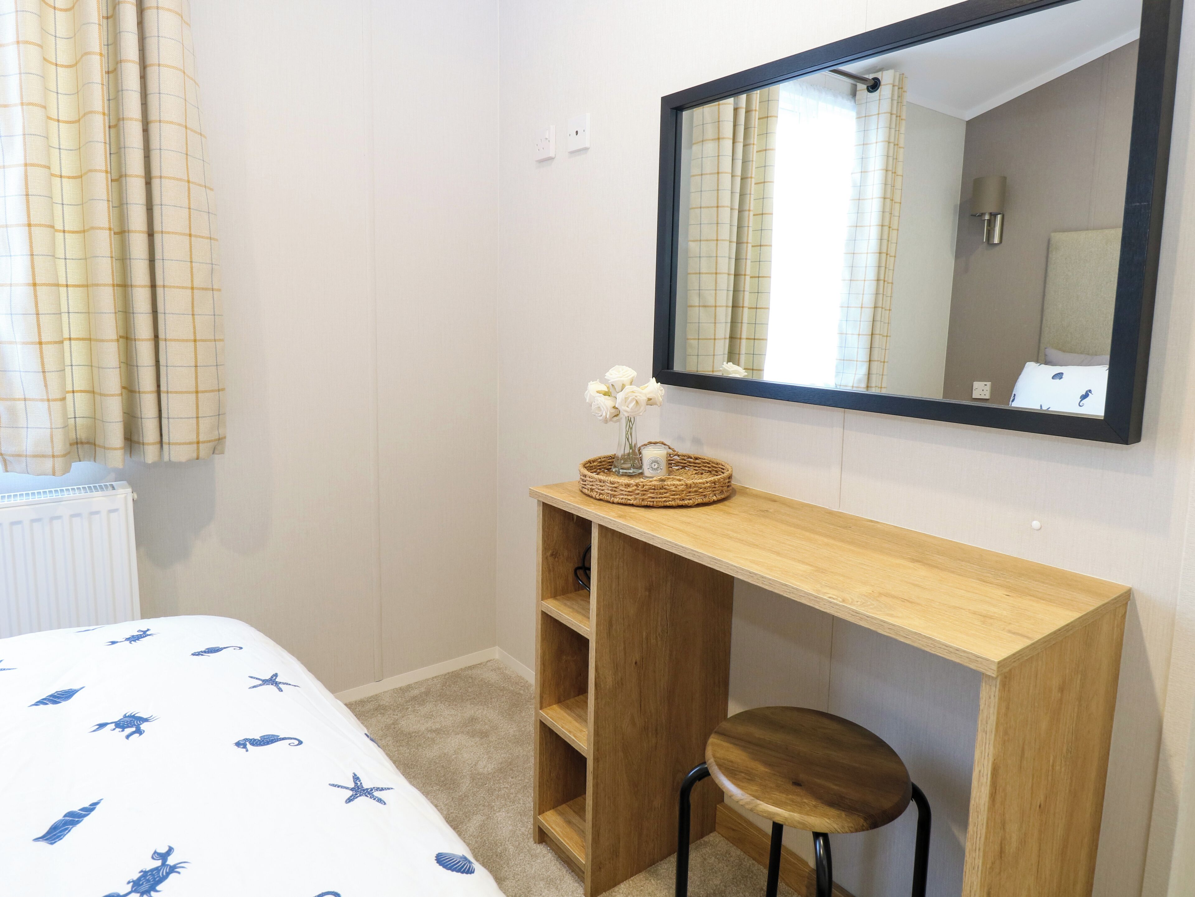 A bedroom with a bed, a wooden desk, a chair, a mirror, and a radiator.