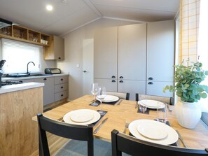A dining area with a wooden table set for four, a kitchen with a built-in stove, and a potted plant on the windowsill. - The Sea Lodge (Norwich)