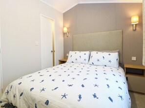 A bedroom with a bed, two bedside tables, a nightstand, a door, and two wall-mounted lamps. - The Sea Lodge (Norwich)