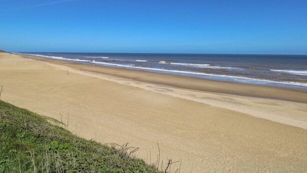 A wide sandy beach with gentle waves and a clear blue sky. - The Sea Lodge (Norwich)