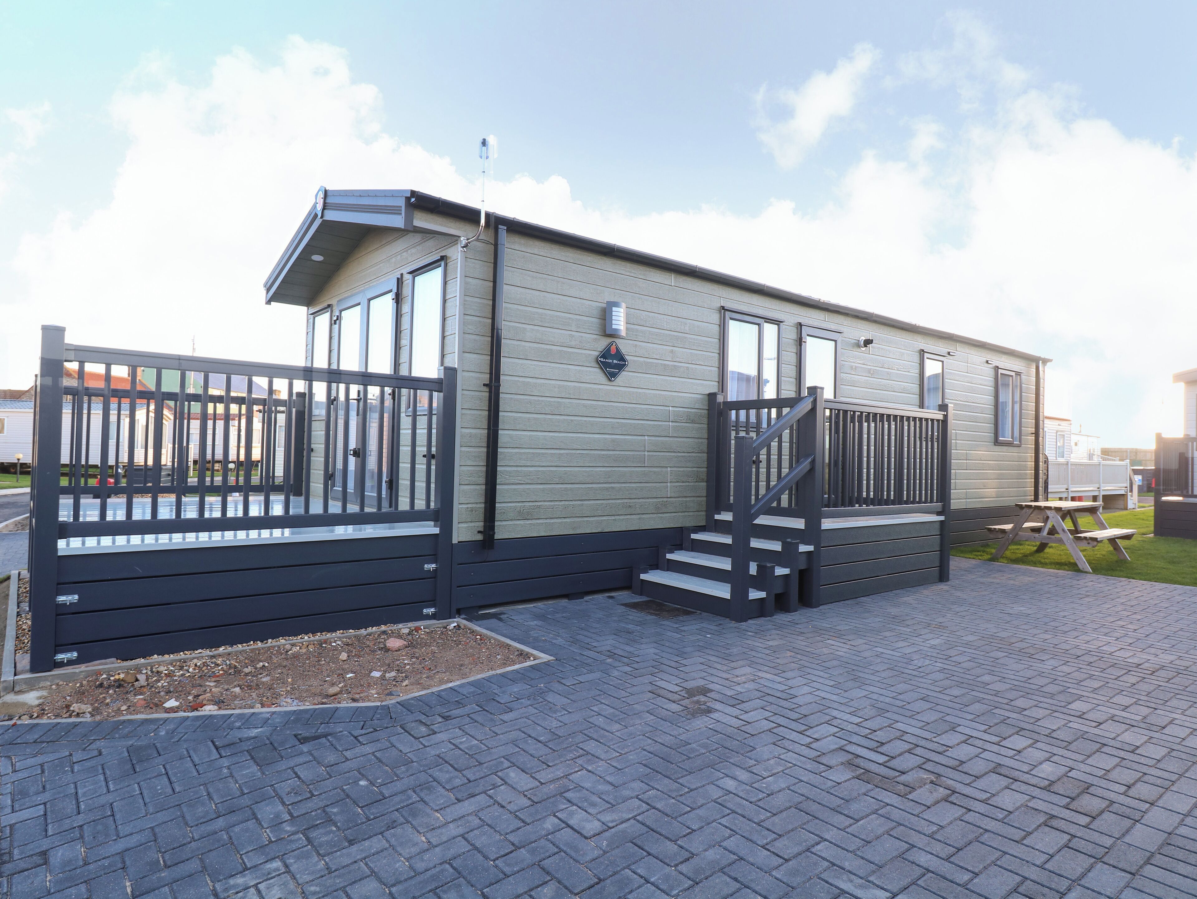 A single-story mobile home with a front porch, a staircase, and a fenced driveway.