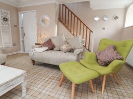 Uma sala de estar com sofá, poltrona verde, mesa branca e escada.
