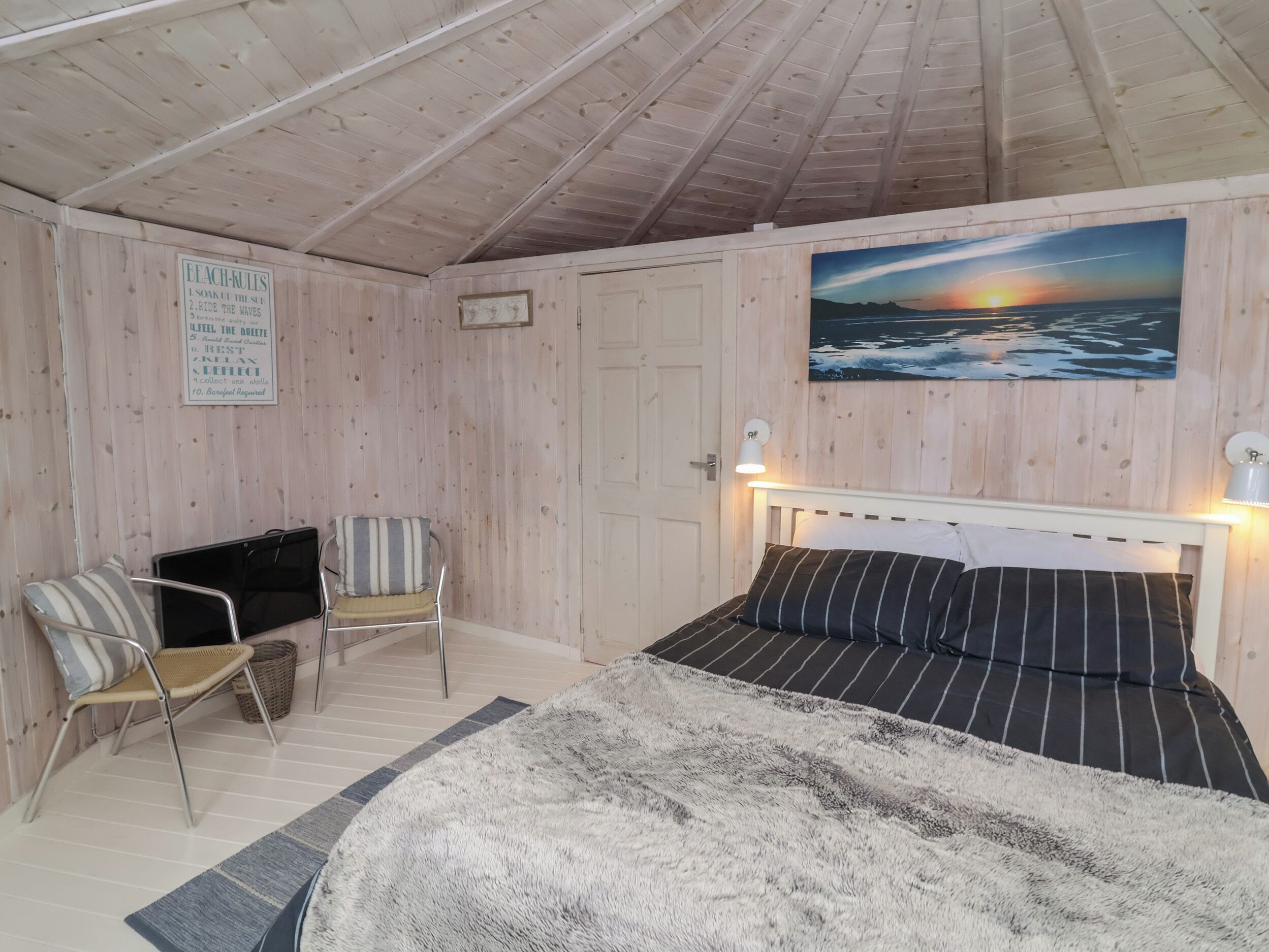 A bedroom with a bed, a chair, a painting of a sunset, and a sign on the wall.