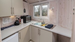Une cuisine compacte avec des meubles en bois, un four à micro-ondes, une bouilloire et un évier situé sous une fenêtre.