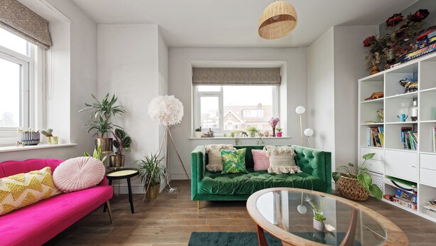 A modern living room with a green sofa, a pink couch, a glass coffee table, and a bookshelf filled with books and decorative items. - Walpole Bay Sea Views (Margate)