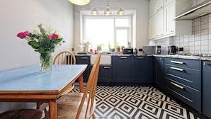 A modern kitchen with dark blue cabinets, a patterned floor, and a wooden dining table with chairs. - Walpole Bay Sea Views (Margate)
