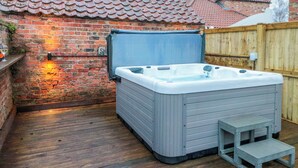 A hot tub in a backyard with a brick wall, wooden deck, and a wooden fence. - The Old Post Office (York)