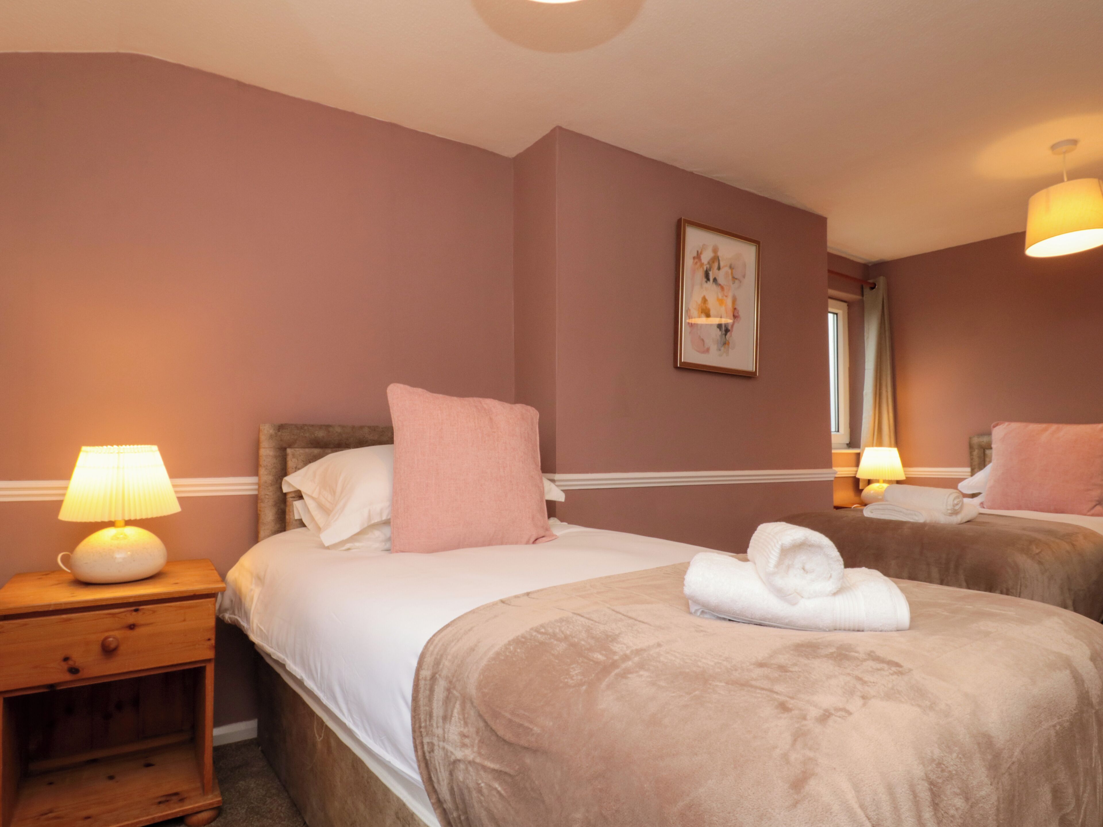 Een hotelkamer met twee bedden, een nachtkastje met een lamp, een schilderij aan de muur en een raam met gordijnen.